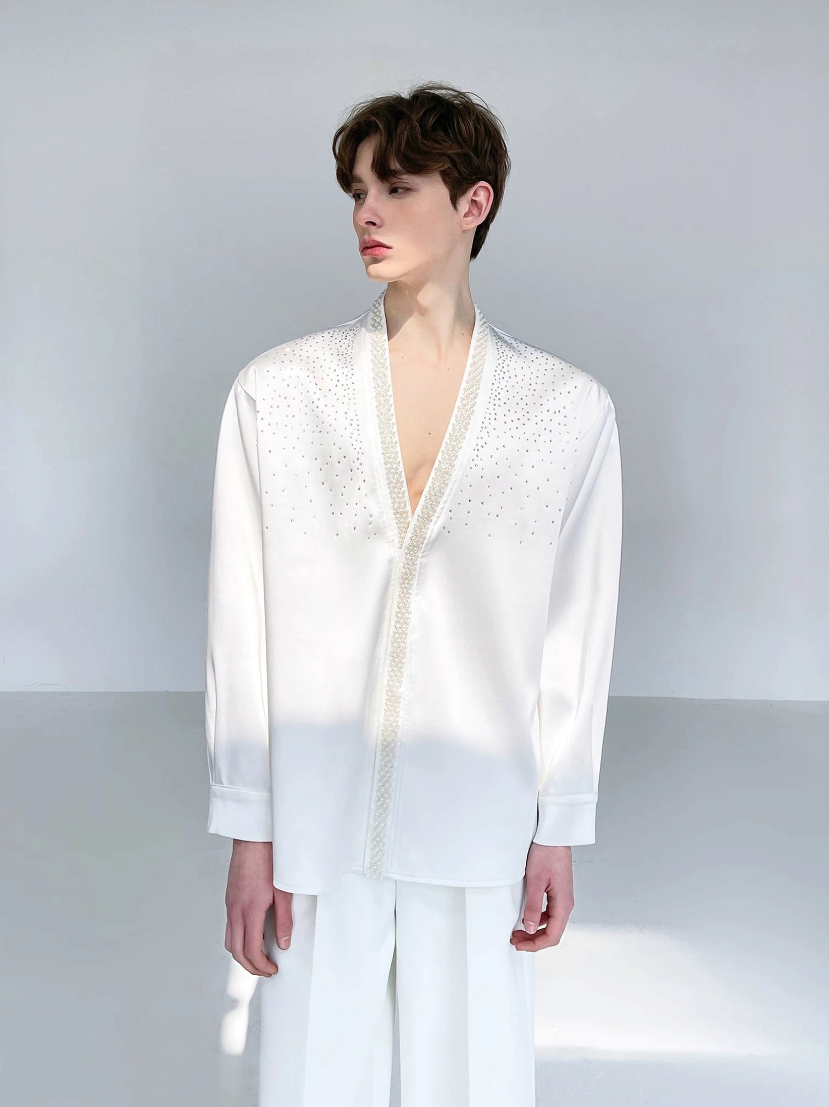 Men's ivory satin shirt styled with relaxed wide-leg white trousers in a clean monochrome Korean streetwear outfit viewed from the side and back