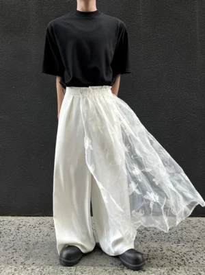 Three-quarter view of ivory satin wide-leg trousers featuring a flowing floral embroidered sheer overlay