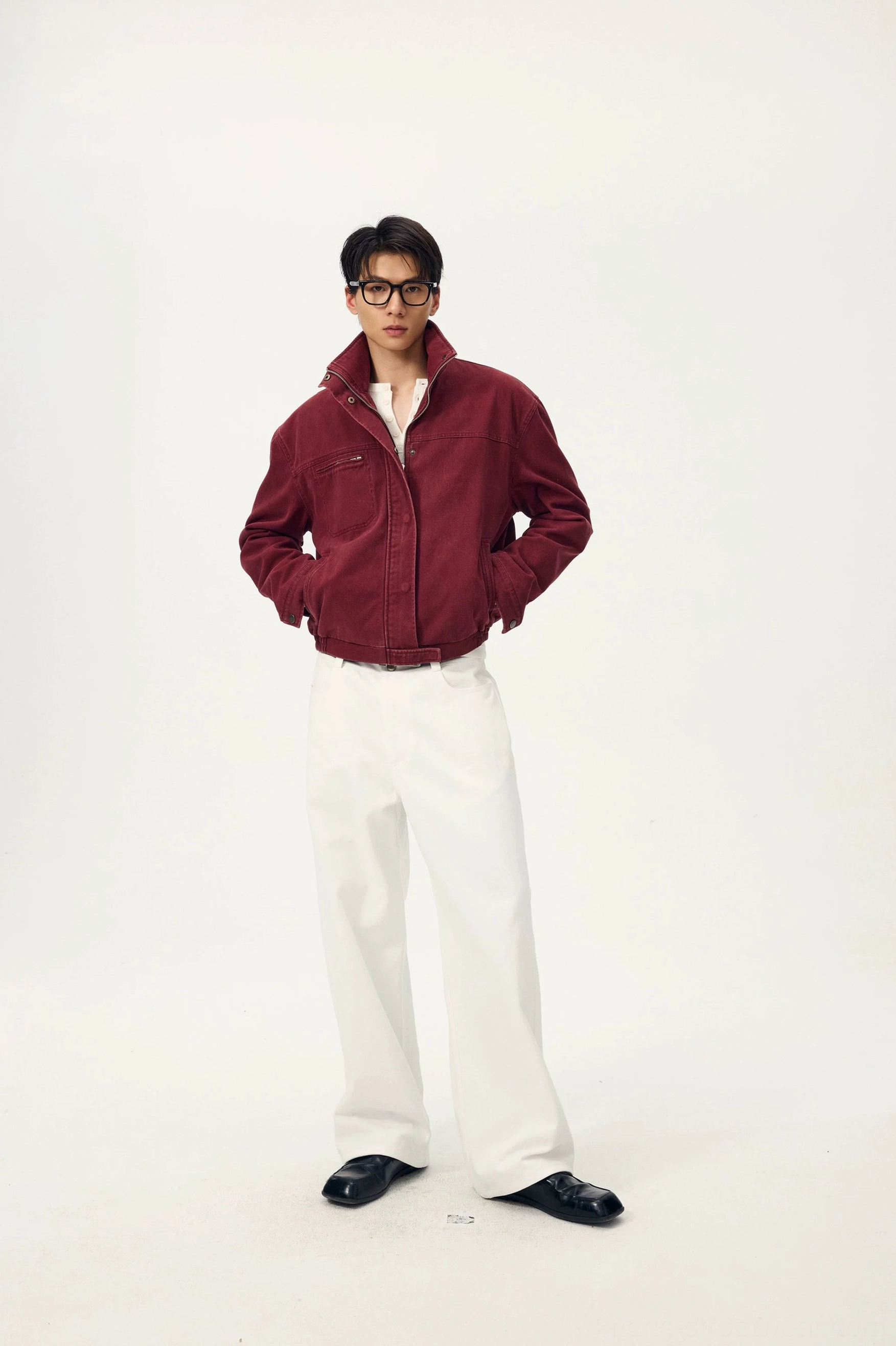 Male model wearing ivory white wide-leg streetwear trousers with a burgundy cropped stand-collar jacket and glasses