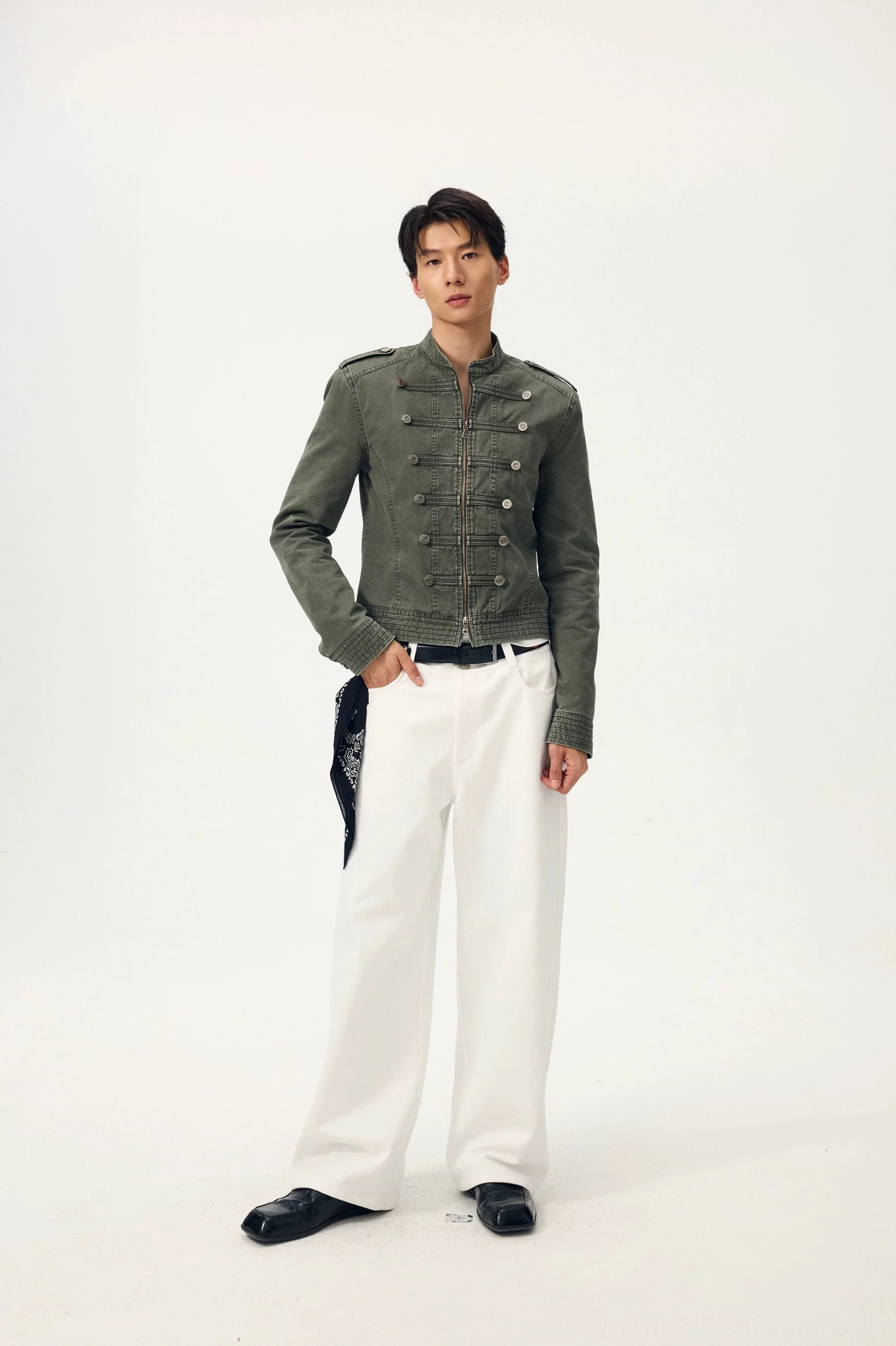 Male model styling ivory white wide-leg trousers with an army green cropped military jacket, black belt, and waist bandana