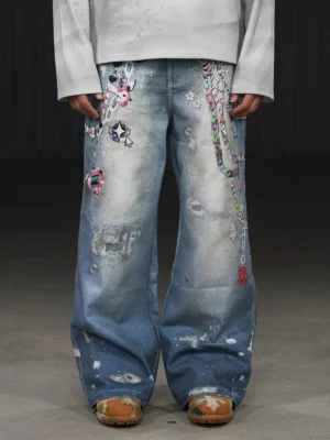 Low-angle front view of faded blue kawaii chain distressed wide leg streetwear jeans with colorful charms, cartoon graphics, ripped denim and white paint splatters