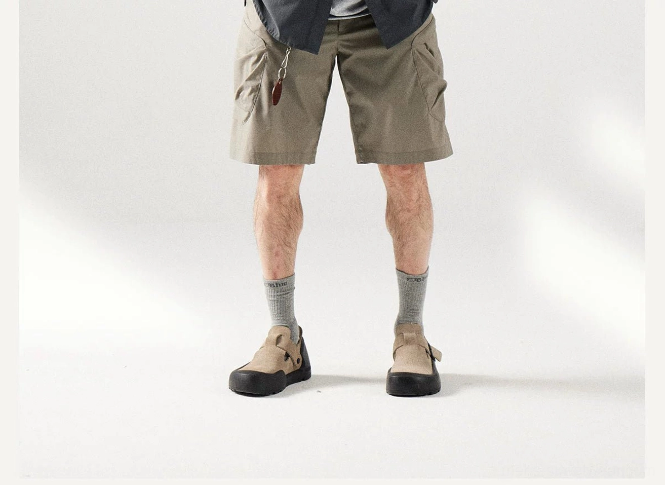 Front lower view of loose fit khaki cargo shorts featuring a small zippered waist pocket and practical utility styling