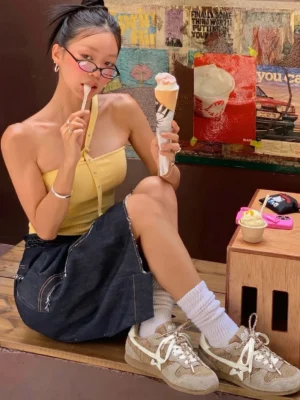 Female model wearing khaki mesh star German trainer sneakers with a retro casual streetwear outfit at an outdoor dessert shop