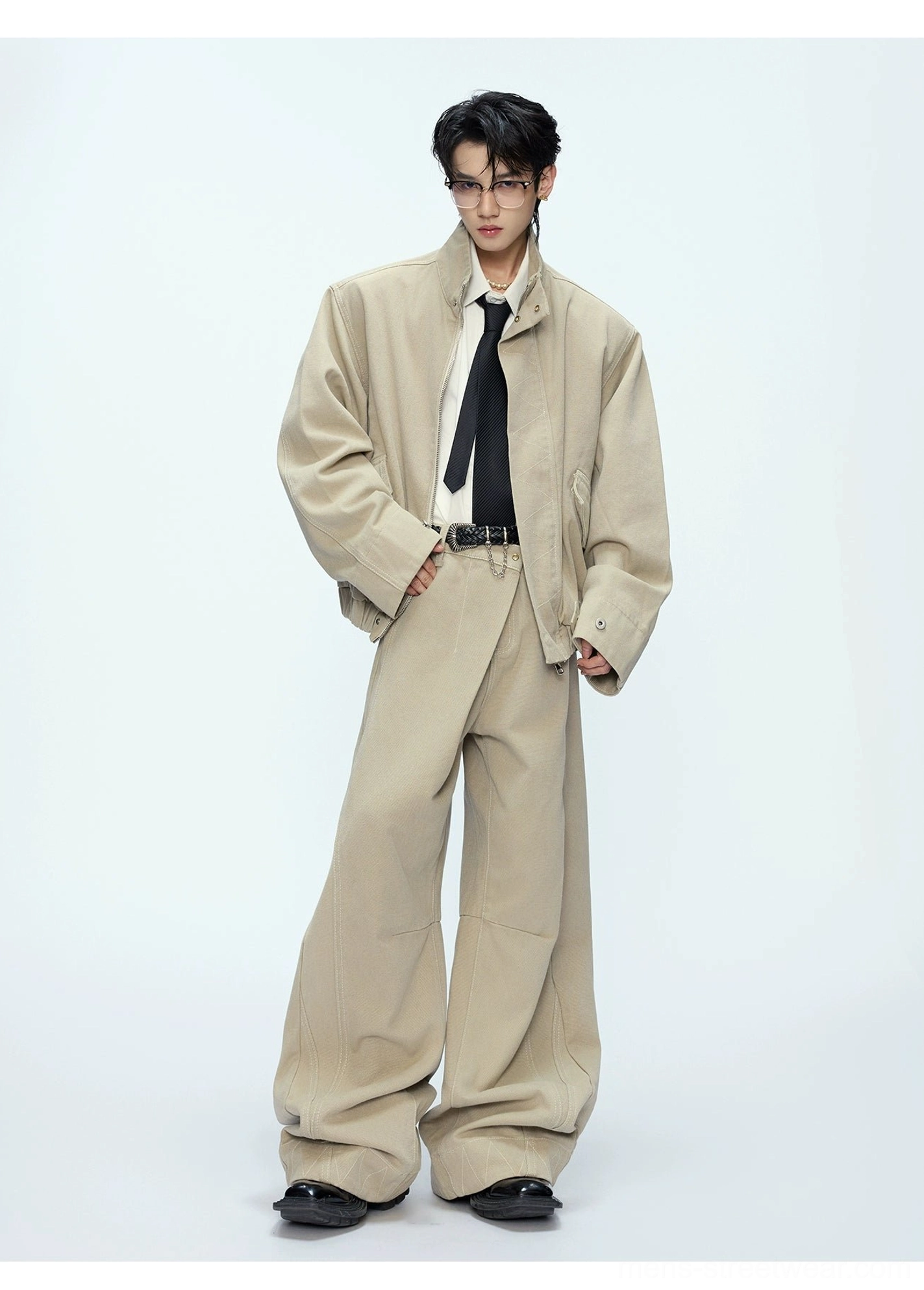 Khaki oversized bomber jacket and wide-leg trousers full front three-quarter view styled with white shirt black tie and leather belt