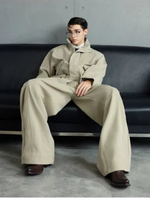 Khaki oversized cotton bomber jacket and wide-leg trousers streetwear outfit photographed seated in a concrete studio