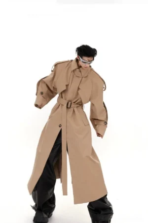 Khaki oversized shoulder pad trench coat shown from a three-quarter front view with belted waist, wide structured shoulders, buttoned cuffs, leather trousers, and futuristic sunglasses