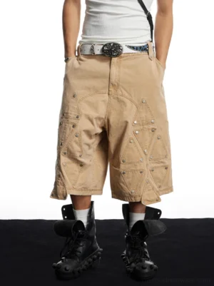 Front low-angle view of khaki rivet panel utility long shorts with oversized wide-leg streetwear silhouette and geometric front pocket details