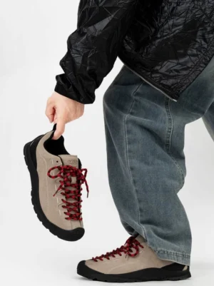 Khaki suede low-top trail sneakers with burgundy hiking laces and black rubber outsole shown in hand and worn with blue jeans
