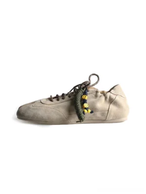 Khaki suede tabi sneakers shown in a front three-quarter studio view with split toe, thin sole, brown laces, and decorative beaded rope lace accessory