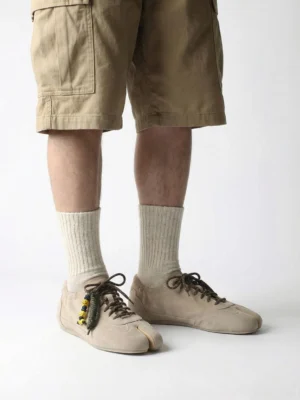 Model wearing khaki suede split-toe tabi sneakers with beige socks and cargo shorts in a relaxed East Asian streetwear outfit