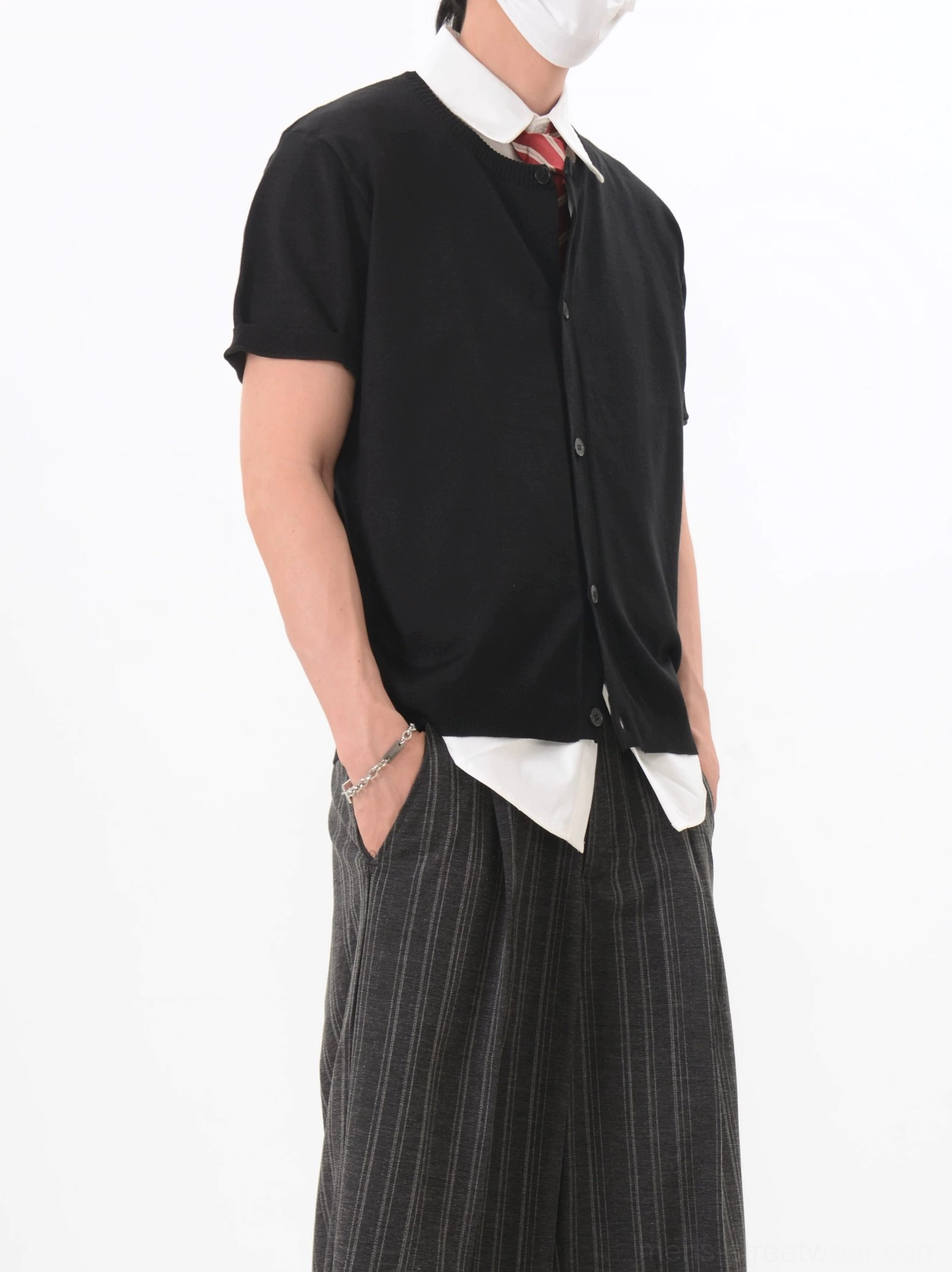 Black short sleeve V-neck knit cardigan side view with exposed white shirt hem and striped wide-leg trousers