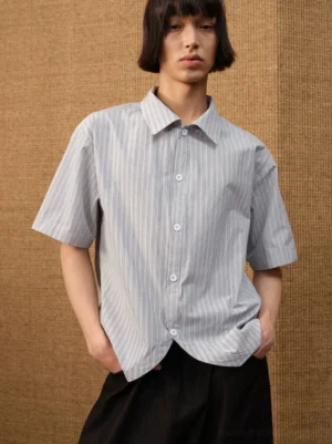 Front close-up of a male model wearing a Korean streetwear white grey pinstripe short sleeve shirt with pointed collar and curved hem