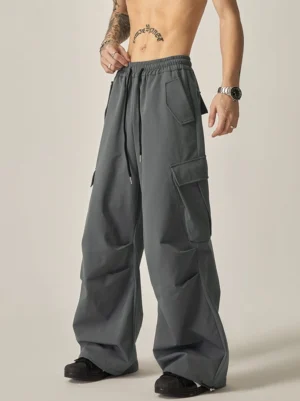 Dark gray Korean streetwear wide leg cargo pants shown from a front three-quarter view with drawstring waist, oversized side pockets, and relaxed matte utility fit