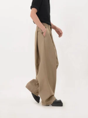 Khaki wide-leg pleated trousers shown from a left rear three-quarter angle with a long draped silhouette and stacked hem over leather shoes
