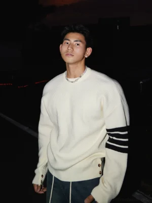 Off-white Korean streetwear crewneck knit sweater with triple black striped sleeve details, loose drop-shoulder fit, side hem buttons, and dark jeans
