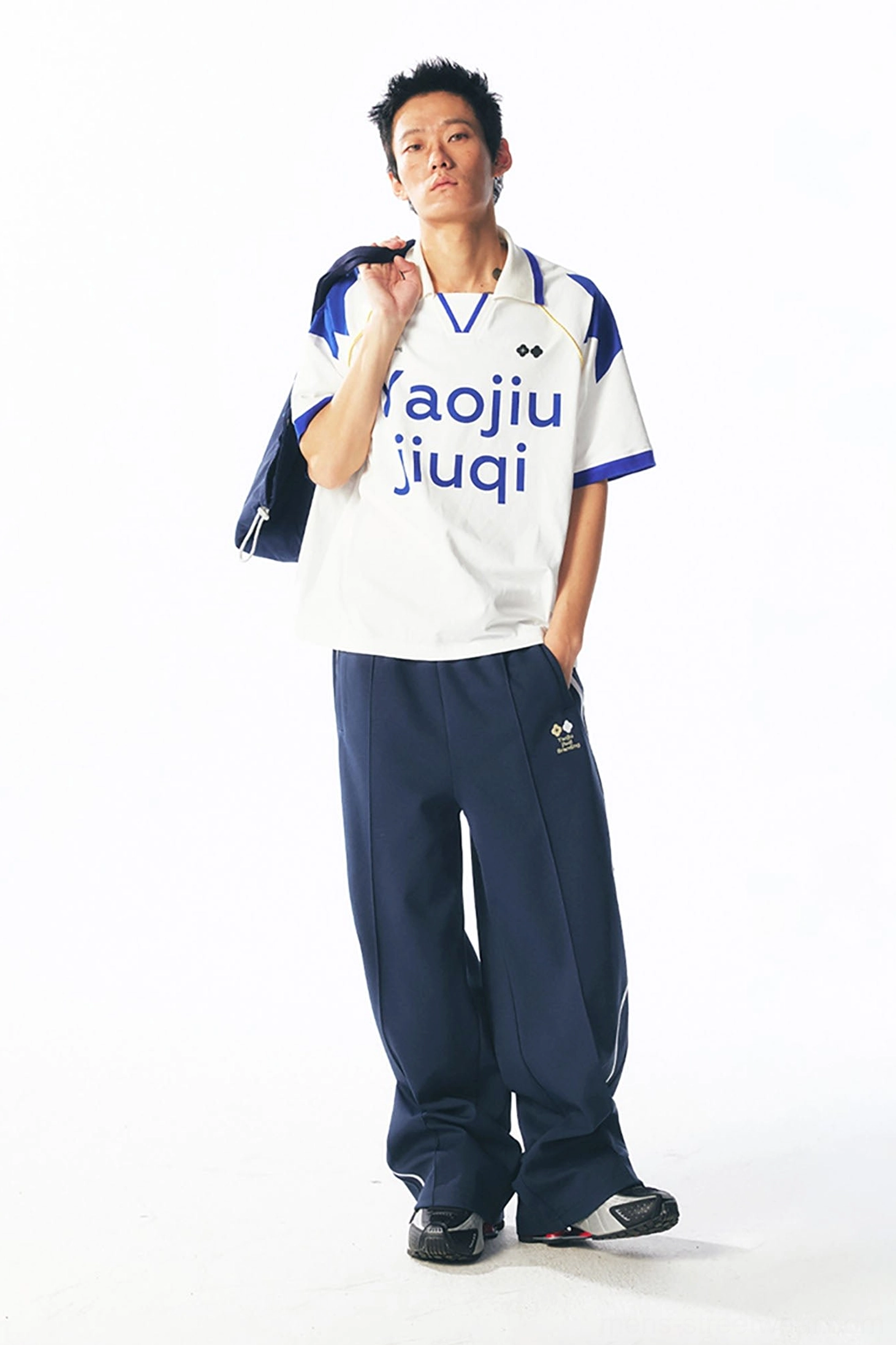 Full-body Korean streetwear outfit featuring a white and blue retro V-neck football jersey, wide-leg navy sport pants, and a dark sports bag