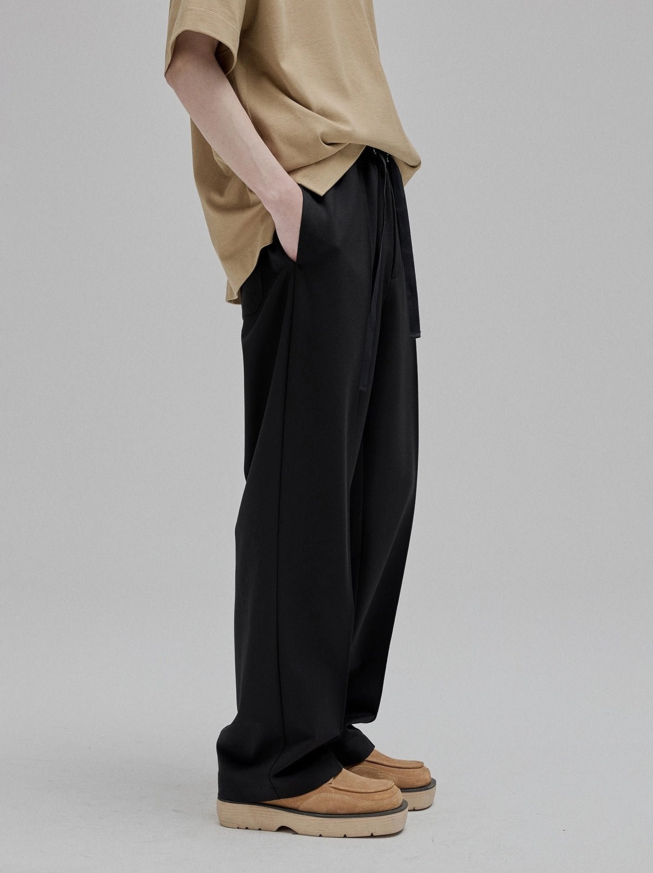 Side view partial lower body of black lace-up straight leg tapered trousers with smooth drapey viscose fabric high-waisted silhouette