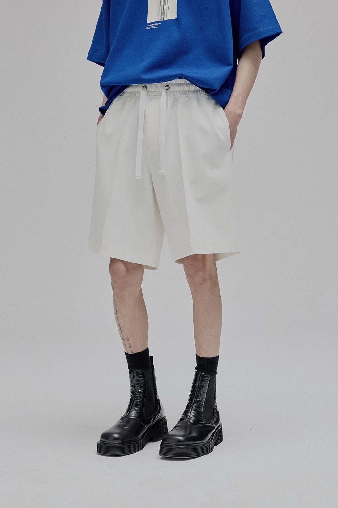 Three quarter front view male model wearing white lace-up straight leg shorts with black combat boots casual streetwear look