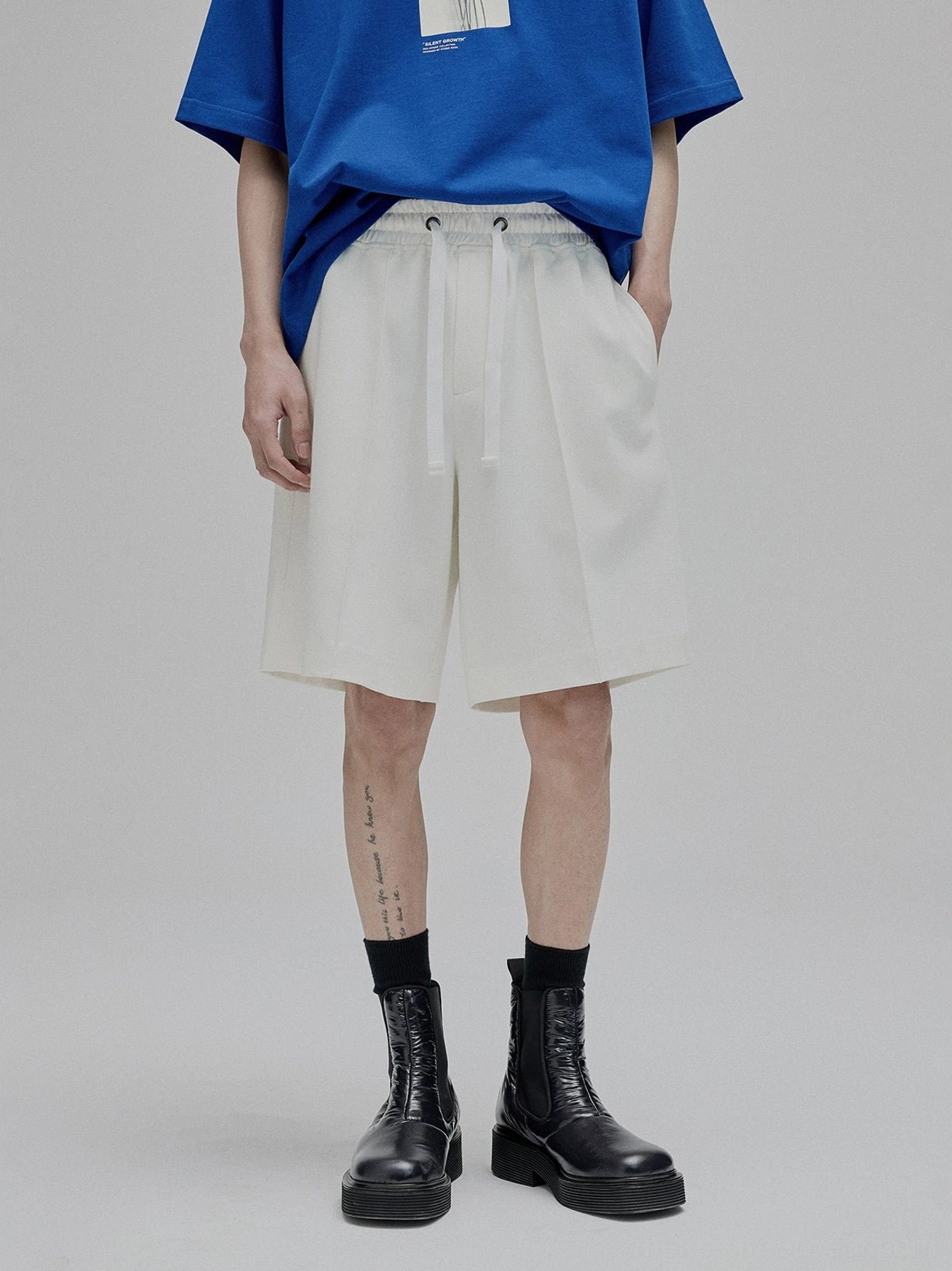 Male model in studio wearing white drawstring lace-up straight leg shorts with solid tee relaxed fit streetwear aesthetic