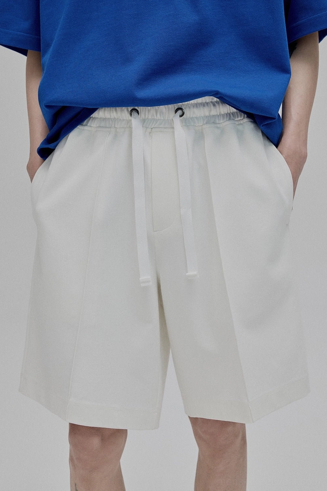 Front close-up partial view white lace-up straight leg shorts with front pleat details dual drawstrings side seam pockets