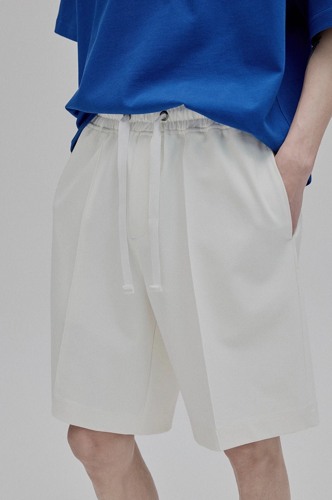 Side partial close-up view white lace-up straight leg shorts with side slip pockets long drawstring details tailored fabric