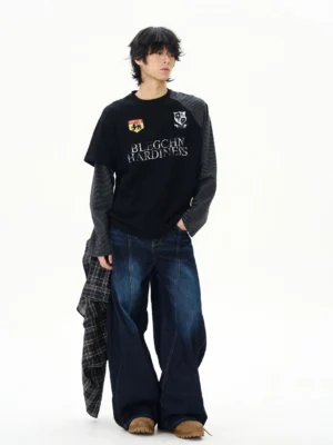 Front three quarter view of a men's layered black varsity long sleeve streetwear tee with striped contrast sleeves and collegiate chest patches styled with wide leg jeans