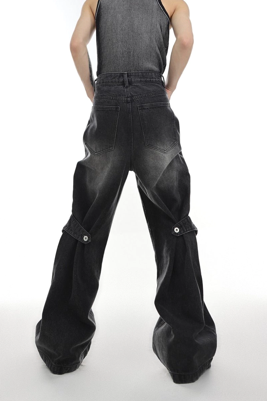 Back view of washed black layered flared denim jeans showing rear pockets side strap and wide flared hem