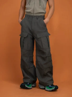 Dark gray layered techwear cargo pants shown from the front three-quarter view with oversized thigh pockets and wide-leg streetwear fit