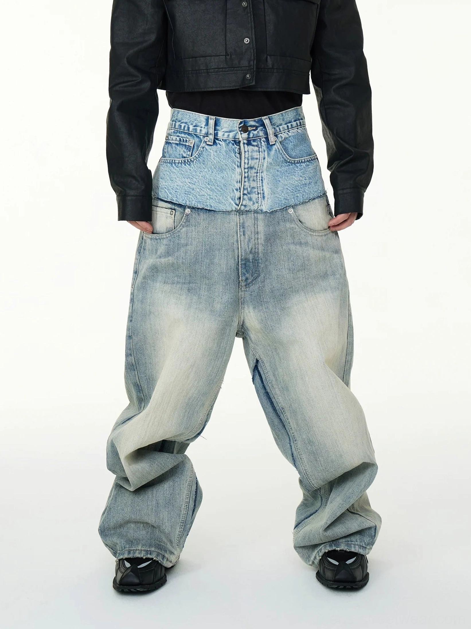 Front full body view of layered two tone high waisted baggy jeans in faded blue denim styled with a black cropped jacket and sneakers