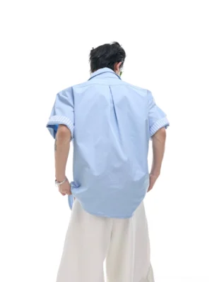 Back view of a light blue layered short sleeve button-up shirt with relaxed pleated back and striped cuff details