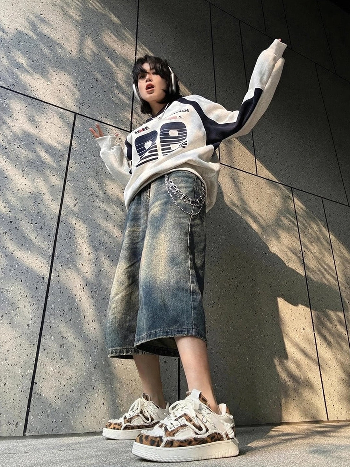 Low-angle view of leopard deconstructed platform sneakers styled with oversized streetwear clothing and cropped denim in outdoor sunlight