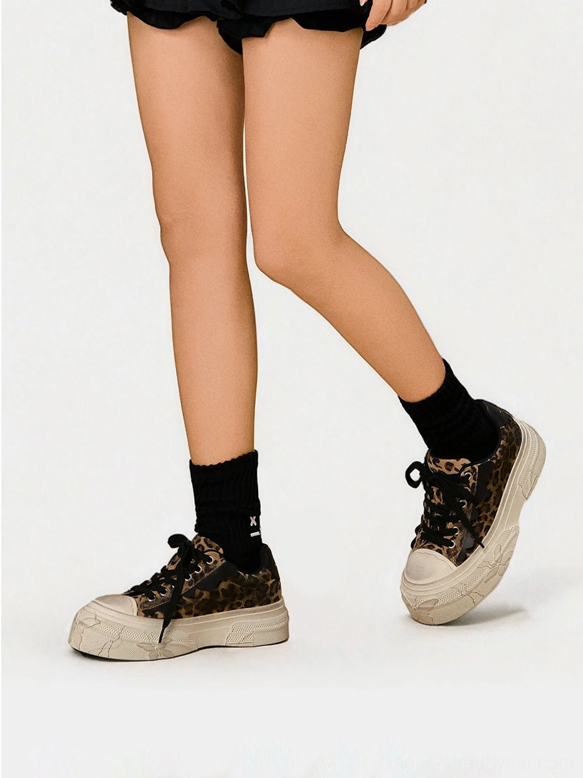 Side view of leopard print low top platform sneakers worn with black mini shorts and black crew socks