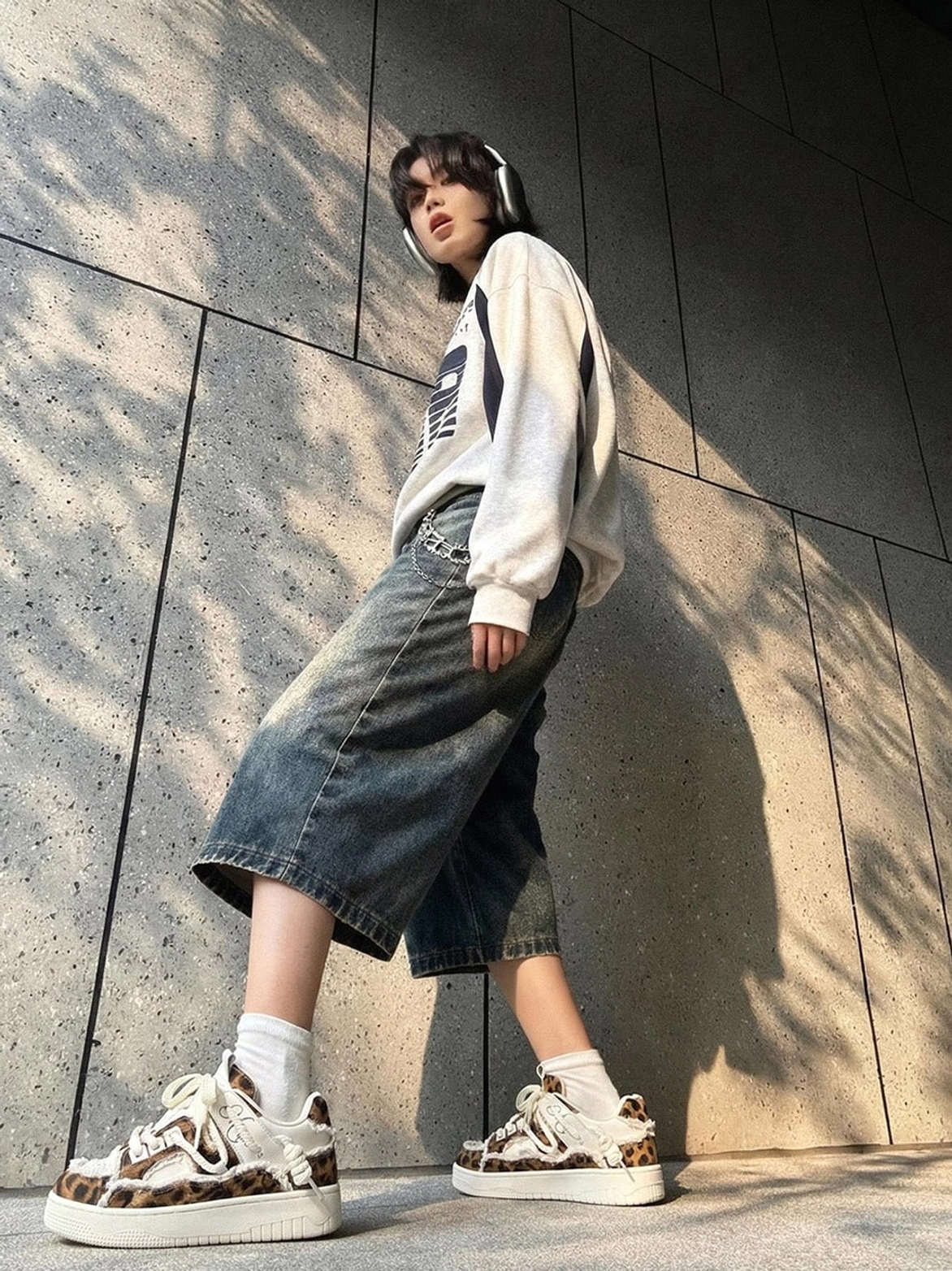 Model wearing leopard platform canvas sneakers with wide-leg cropped jeans oversized graphic sweatshirt and white socks against a sunlit concrete wall