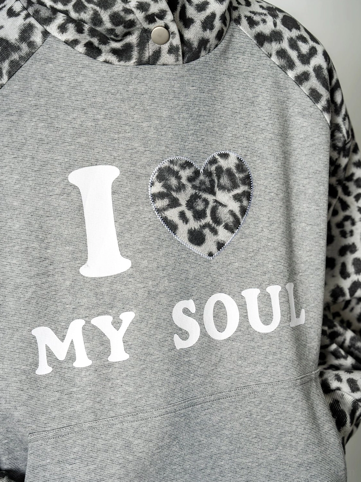 Close-up of heather grey leopard raglan hoodie showing leopard print shoulder panels, snap button hood collar, and I Love My Soul graphic