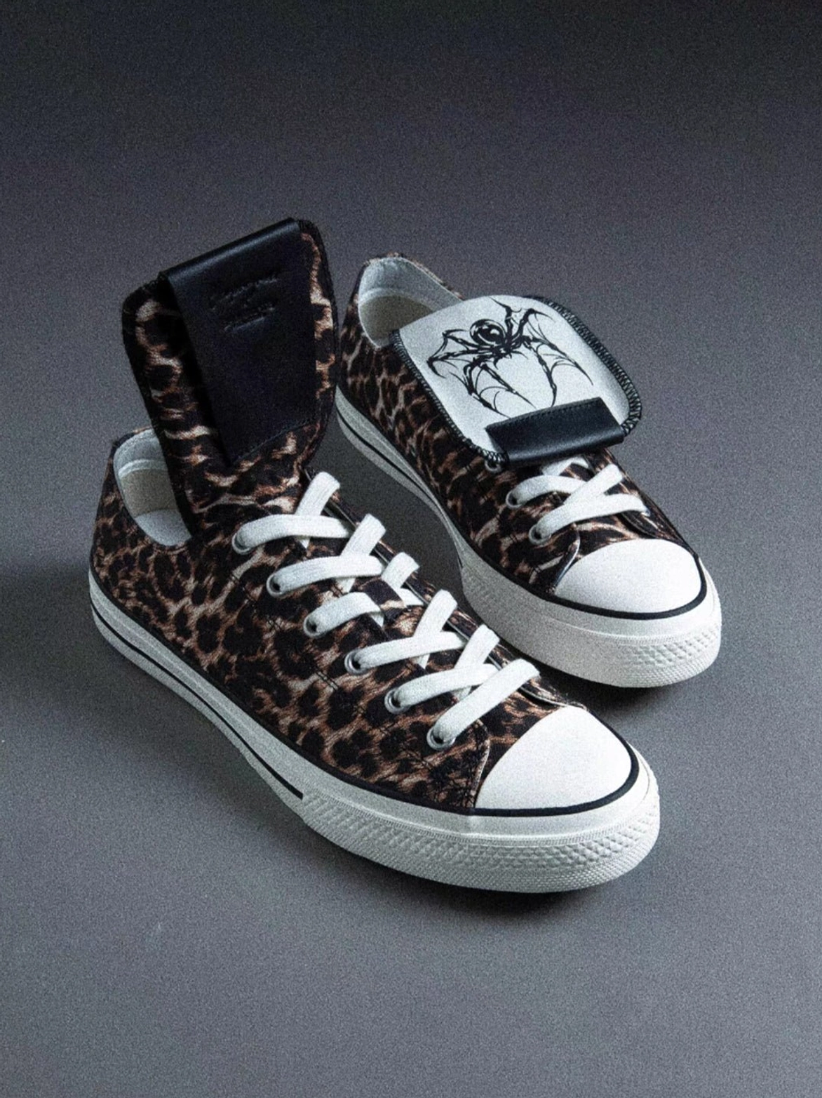 Pair of leopard print low-top canvas sneakers with embroidered foldable spider tongues, white rubber toe caps, and matching flat soles