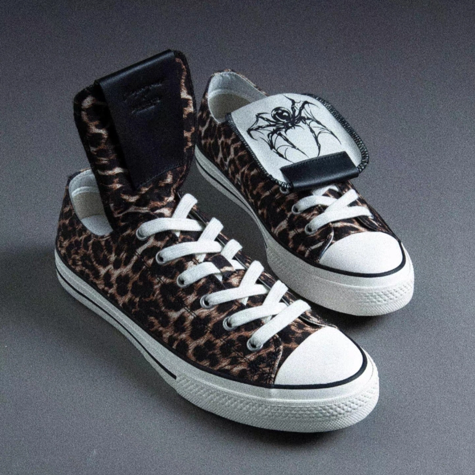 Pair of leopard spider-tongue canvas sneakers shown from above with foldable tongue, black leather patch, white toe caps, and rubber soles