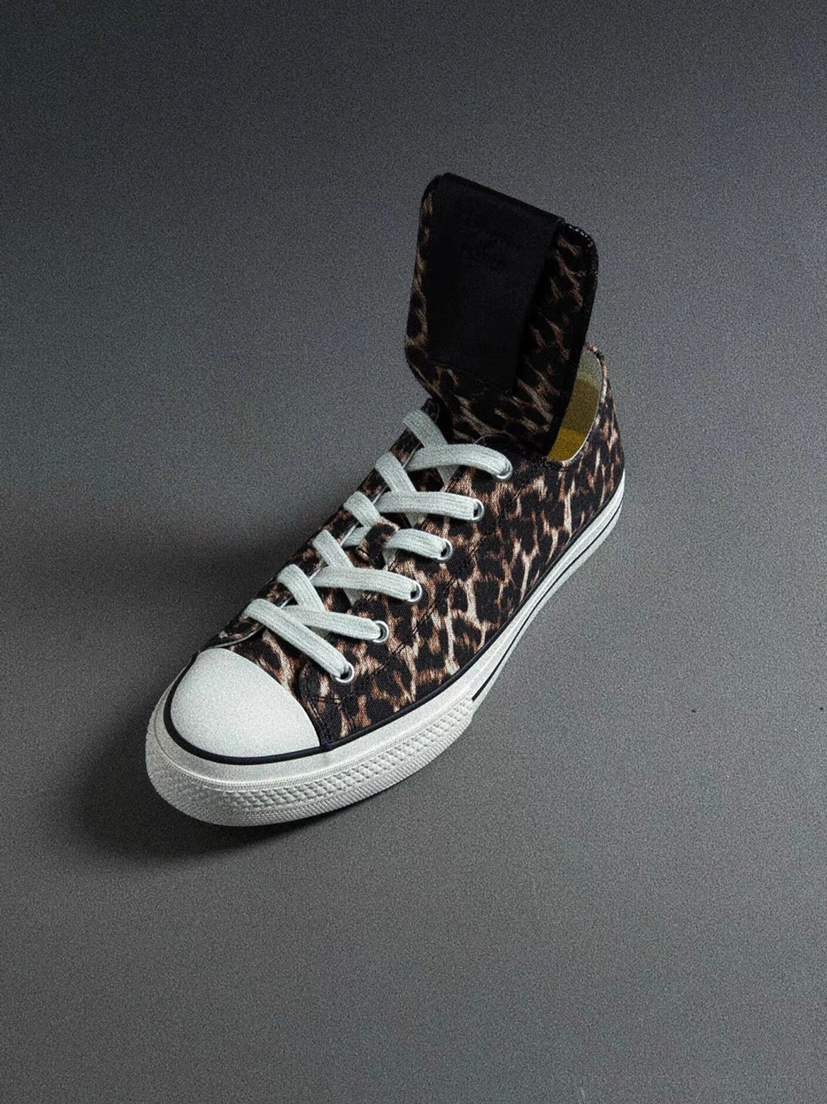 Side view of a leopard spider-tongue canvas sneaker with upright foldable tongue, standard laces, white rubber toe cap, and midsole