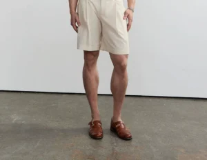 Men wearing light apricot cross-waist linen blend pleated tailored shorts in a minimalist studio front view