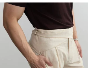 Close-up of light apricot pleated shorts showing cross-over waistband adjustable side tab and front pleats
