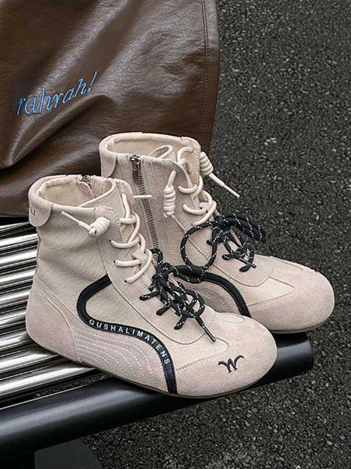 Light beige nubuck suede racing training boots with black contrast stripe, dual laces, and side zipper displayed on a metal bench