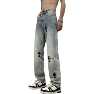 Three-quarter view of light blue washed cross patch wide leg jeans showing black cross appliques, splatter accents, high-rise streetwear silhouette, and relaxed straight-leg cut