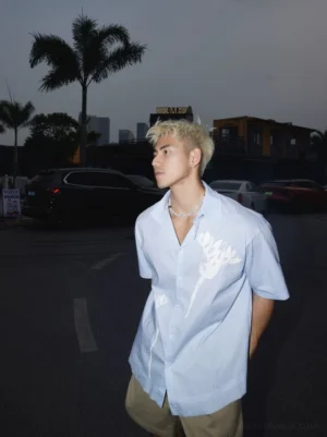 Side view of light blue floral stripe relaxed short-sleeve button-up shirt in an outdoor urban parking lot at dusk