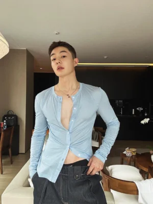 Front view of a men's light blue slim fit cotton button-up shirt styled with dark denim in a modern apartment