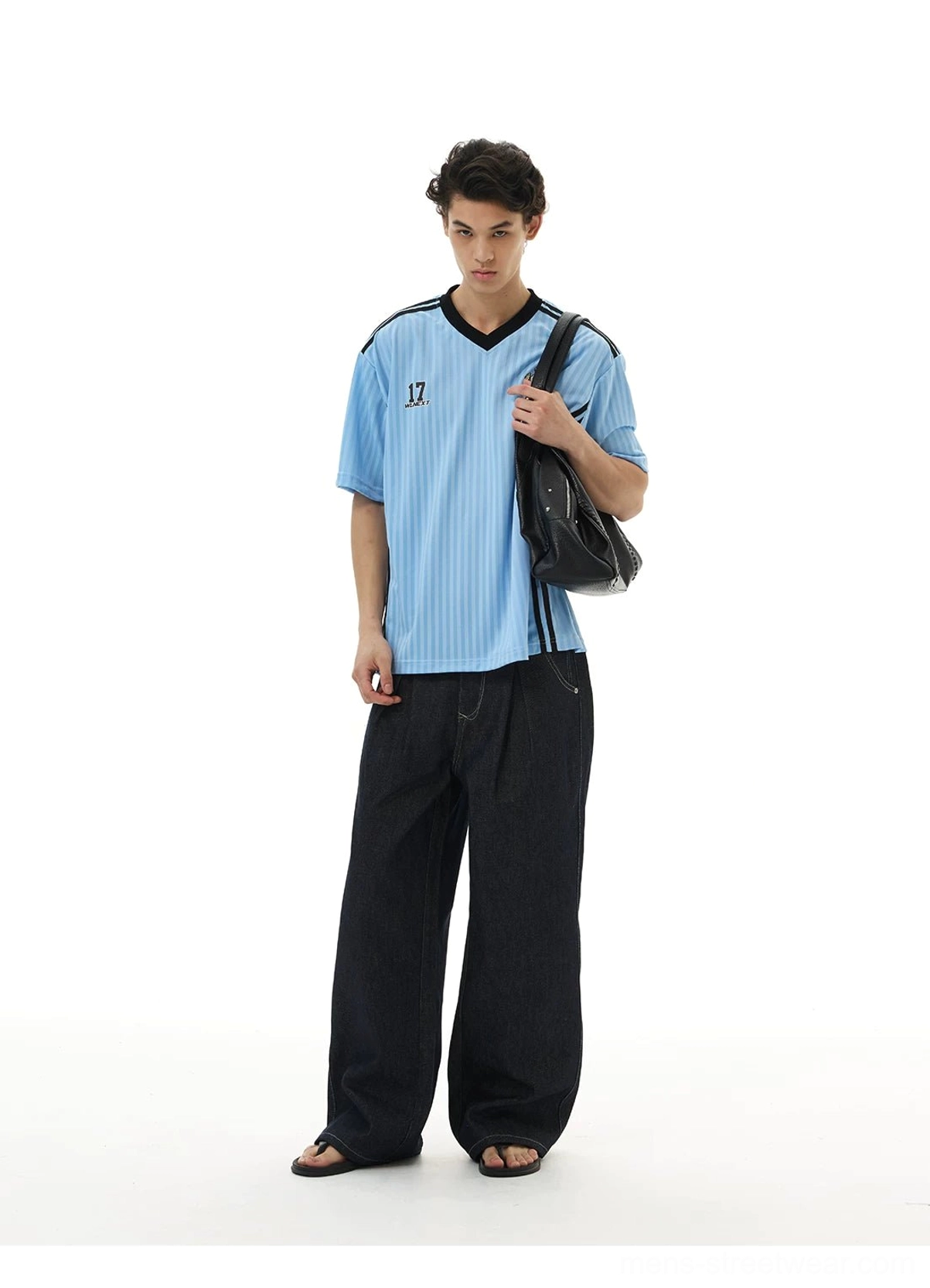 Light blue soccer jersey streetwear tee styled with a shoulder bag, dark wide-leg denim, V-neck trim, and sporty chest graphic