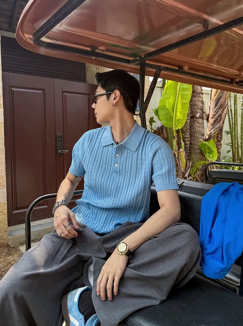 Light blue textured knit polo shirt with classic collar styled with dark grey wide leg trousers in an outdoor villa setting
