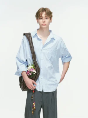 Light blue vertical stripe Korean streetwear overshirt shown in a relaxed three-quarter view with grey wide-leg trousers and a brown leather shoulder bag