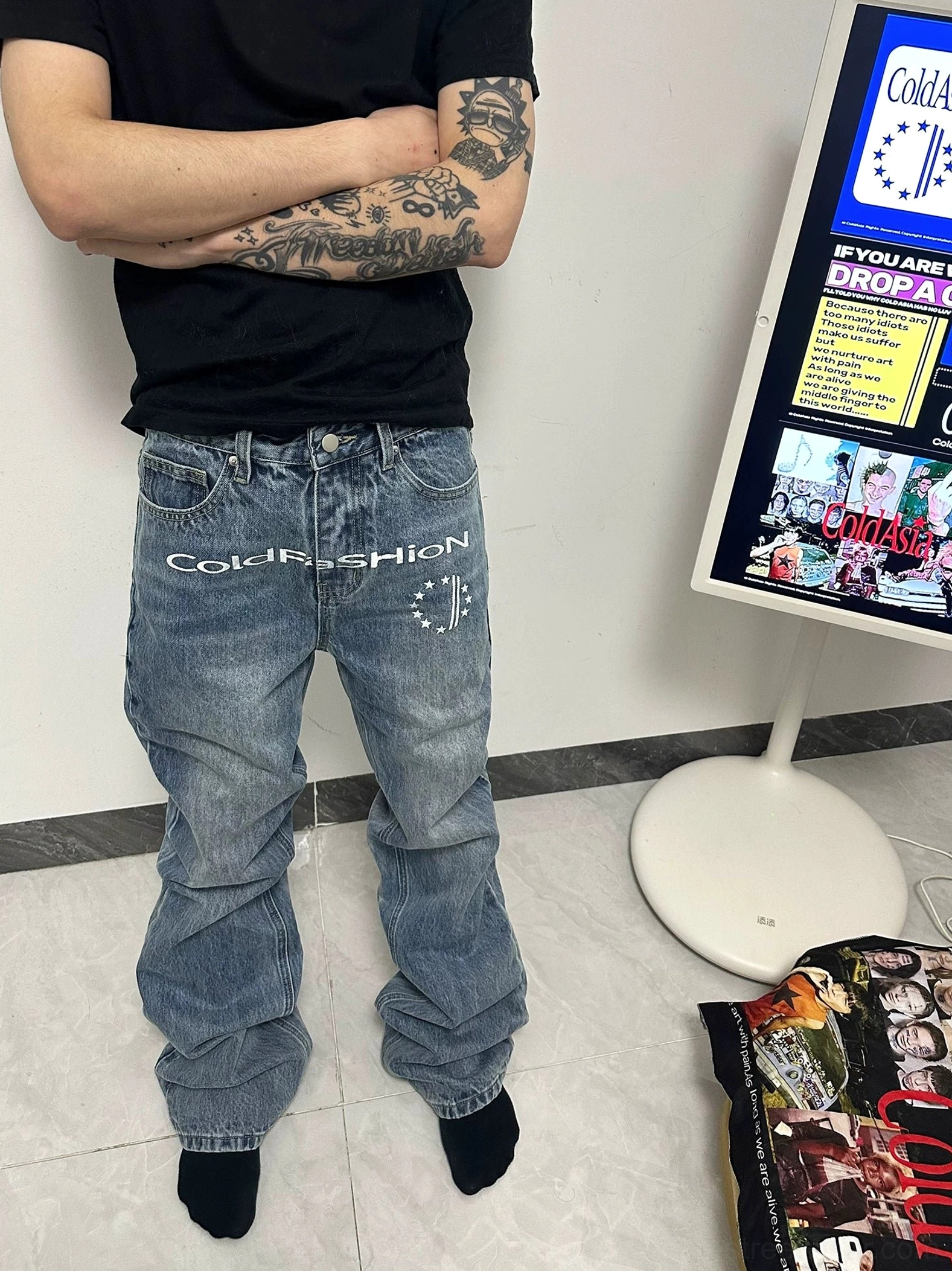 Tattooed male model in light blue vintage flare denim jeans with front graphic and stacked raw hem in studio styling