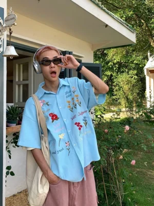 Light blue waffle embroidered floral short sleeve streetwear shirt worn by male model outdoors with sunglasses and headphones