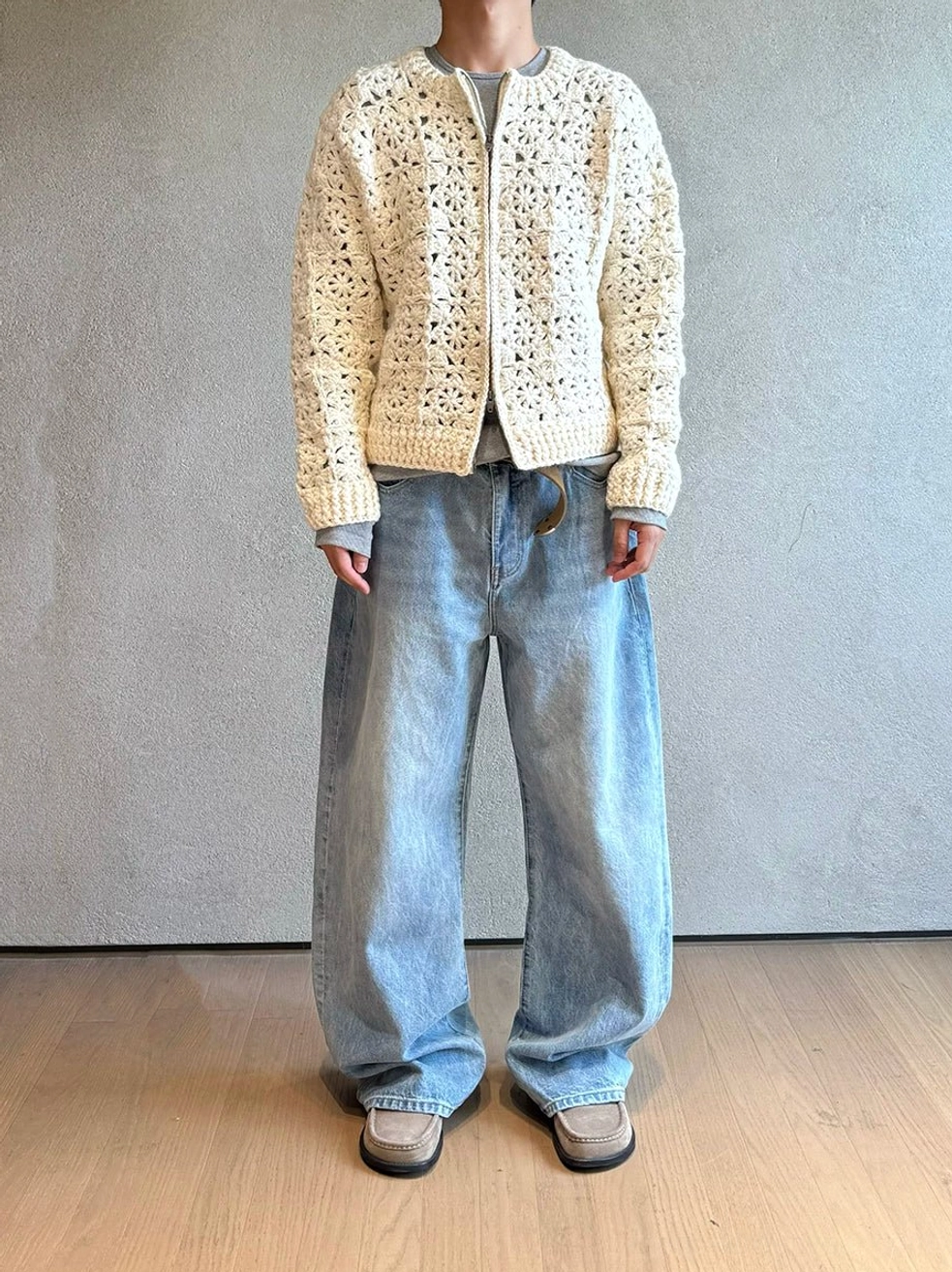 Men's relaxed light blue wide leg jeans paired with a cream crochet cardigan and gray tee in a Korean-inspired streetwear outfit