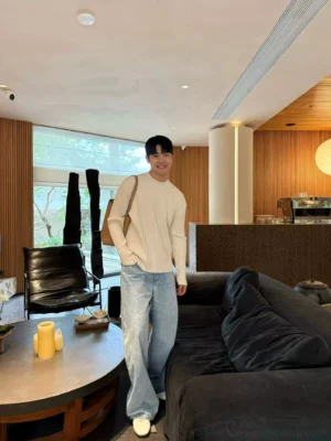 Light blue wide leg denim jeans worn with a ribbed long-sleeve top, white sneakers, and crossbody bag in a modern living room